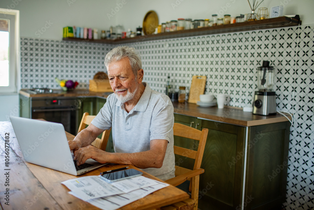 Stressed senior man reading bills on kitchen table with laptop Stressed senior man reading bills on kitchen table with laptop