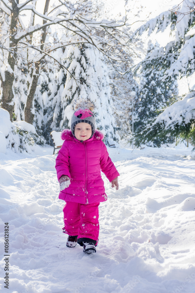 Little girl in pink clothing is running through the snow in a winter park. Winter fun for children. Snow has fallen. Little girl in pink clothing is running through the snow in a winter park. Winter fun for children. Snow has fallen.