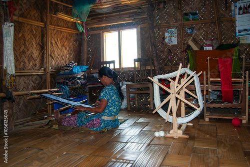 South asian tribal woman working on a handloom machine sitting inside her home photo