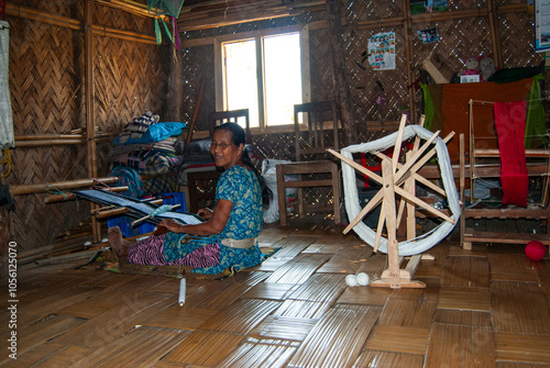 South asian tribal woman working on a handloom machine sitting inside her home photo