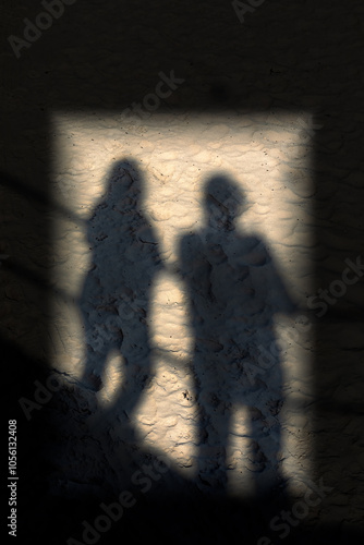 Shadow of people in a door on a well trodden beach of people leaning on railings 