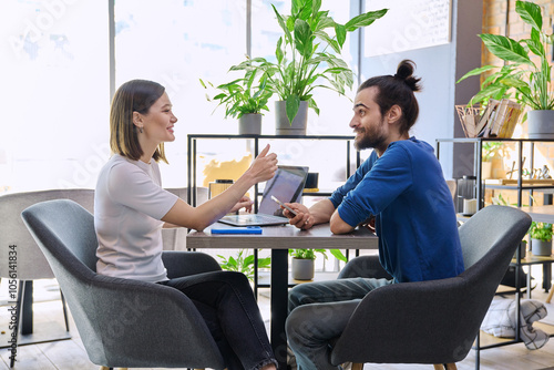 Young man woman sitting at table in coworking space with laptop smartphone, talking together