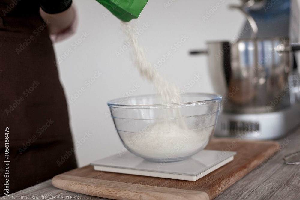 Hand pouring flour into a bowl with a wooden spoon. Using wooden spoon to pour wheat flour into transparent container. Hand pouring flour into a bowl with a wooden spoon. Using wooden spoon to pour wheat flour into transparent container.