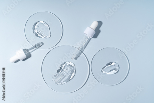 Two pipettes with gel smears on a laboratory circle glass on blue background, sterile cosmetics concept