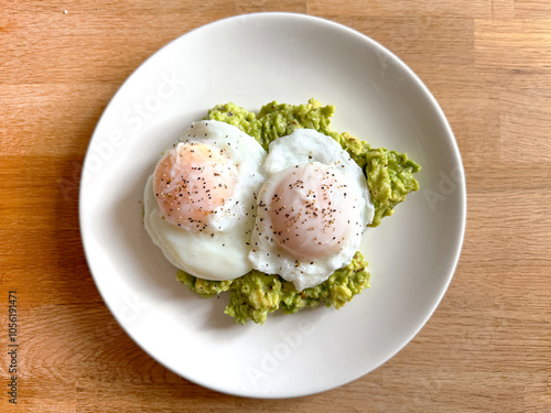 Two poached eggs on smashed avocado on a small round white plate