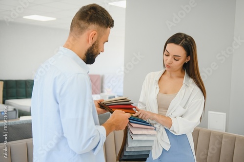 Couple choose soft corner in furniture store. Husband examines set of upholstery fabric samples