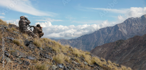 Men in camouflage covertly conduct surveillance high in the mountains.