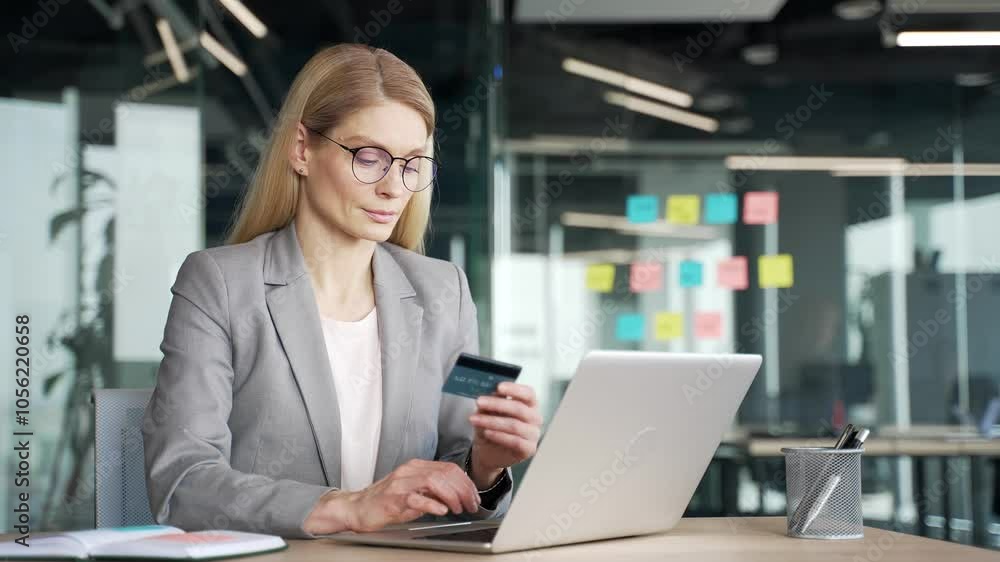Smiling businesswoman enters a credit card number on a laptop while sitting at desk at workplace in a business office. Happy female employee shopping in online store, happy about discounts, promotions Smiling businesswoman enters a credit card number on a laptop while sitting at desk at workplace in a business office. Happy female employee shopping in online store, happy about discounts, promotions