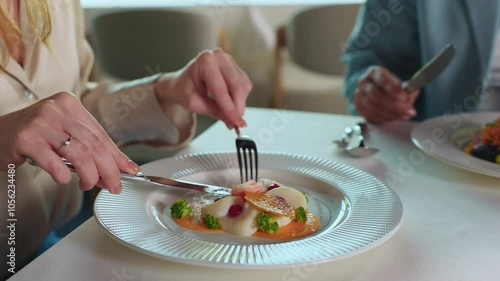 Closeup shot of female hands with neat nails. Footage of attractive young woman with ginger hair in elegant blouse eating beautiful delicious meal in restaurant during dinner with mother. Indoors