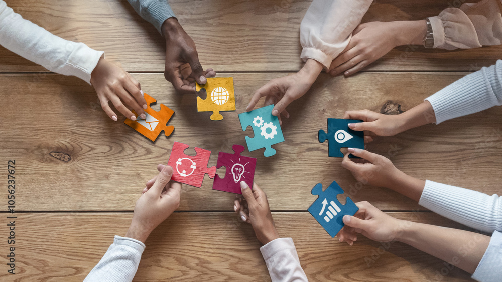 © Prostock-studio - International team of coworkers sitting around table, putting colorful puzzles together, teamwork concept, top view