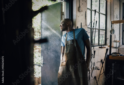 Happy male craftsperson with hands in pockets looking outside workshop photo