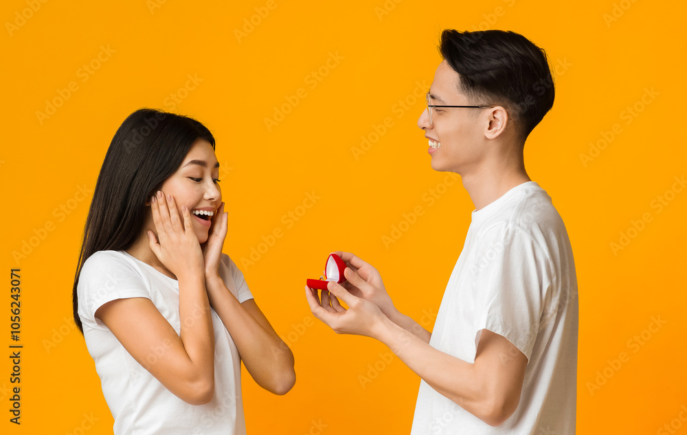 Asian young man in love making proposal to his amazed girlfriend, orange background Asian young man in love making proposal to his amazed girlfriend, orange background