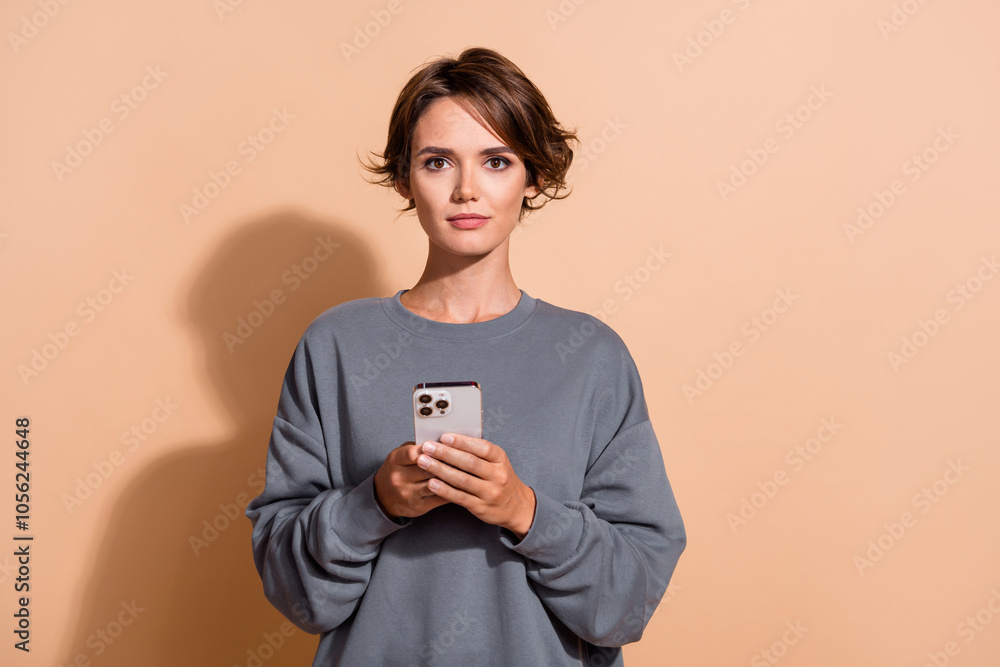 Portrait of serious pretty girl with bob hairstyle wear pullover hold smartphone read notification isolated on beige color background Portrait of serious pretty girl with bob hairstyle wear pullover hold smartphone read notification isolated on beige color background