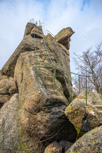 Visitors can climb the steep stairs of the Oresnik granite rock formation in Hejnice, offering stunning views from the lookout point and a wooden summit cross against a cloudy sky. photo