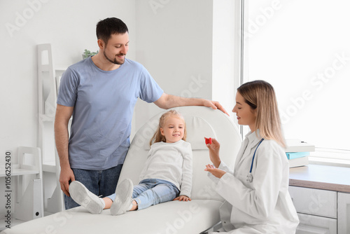 Female endocrinologist showing thyroid gland model to little girl and father in clinic