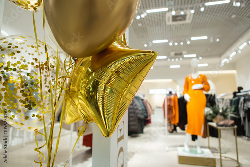 In a vibrant store, numerous shiny gold balloons float cheerfully, while a stylish mannequin stands prominently in the background, catching the eye