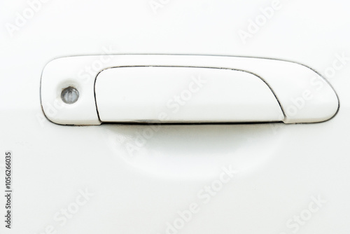 View of a used white car door handle. handle itself is a rectangular shape with a slight curve at the bottom. Round hole at the top end of the handle likely for a keyhole. Stains in the keyhole. photo