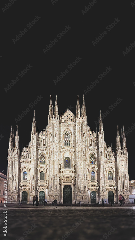 Low angle view of illuminated Milan Cathedral (Metropolitan Cathedral-Basilica of the Nativity of Saint Mary), Italy and its front facade with incidental people at night