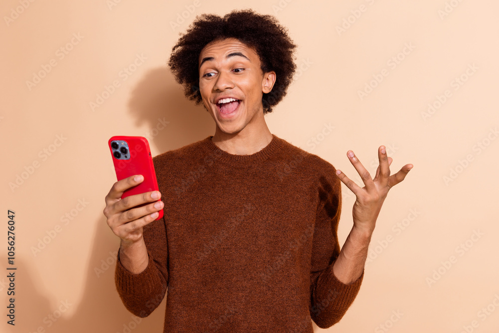 Young man holding smartphone and reacting with excitement and surprise against beige background Young man holding smartphone and reacting with excitement and surprise against beige background