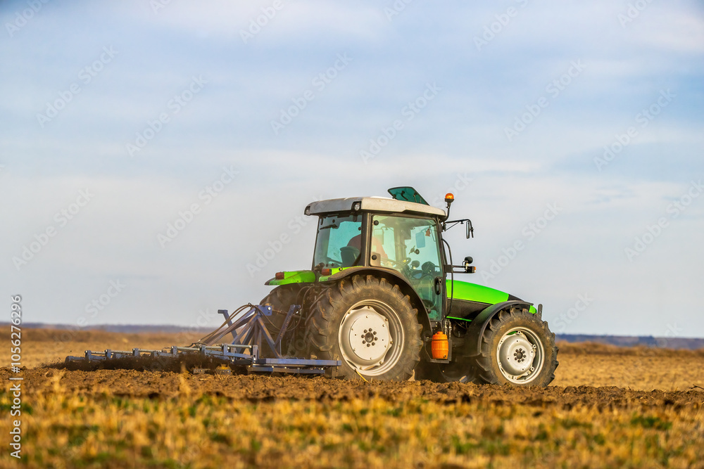 A tractor with plow in action, turning over the soil on a sunny day A tractor with plow in action, turning over the soil on a sunny day