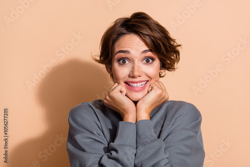 Photo portrait of attractive young woman dreamy posing fists touch cheeks wear trendy gray clothes isolated on beige color background