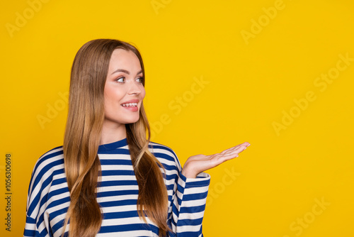 Photo of nice cute woman wear striped stylish sweatshirt arm hold empty space isolated on yellow color background