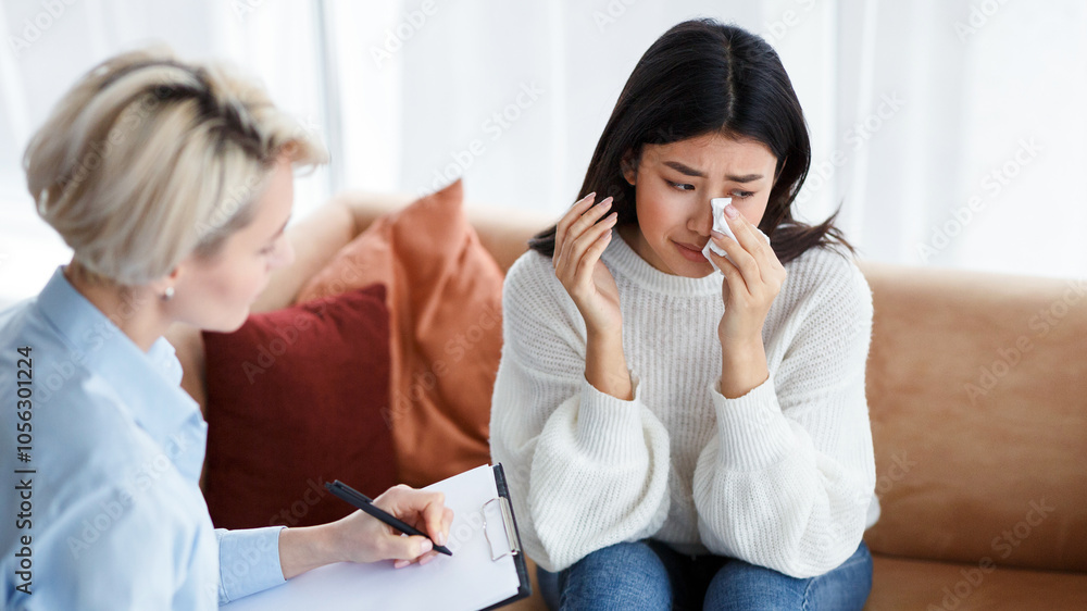 Asian Woman Crying Talking With Psychologist Recovering After Breakup Sitting In Office. Professional Help Concept. Selective Focus Asian Woman Crying Talking With Psychologist Recovering After Breakup Sitting In Office. Professional Help Concept. Selective Focus