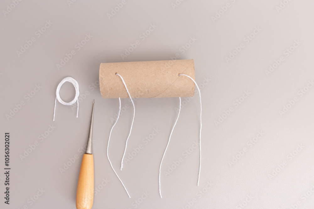 Obraz premium toilet paper cardboard roll tube with threading a string through holes, part of DIY project, moment in the crafting process, highlighting the use of simple tools to alter everyday objects