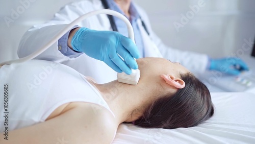 Doctor man wearing blue medical gloves is using ultrasound equipment on neck of female patient lying down for a medical examination photo