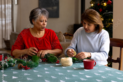 Senior female friends crafting Christmas decorations together at home, enjoying festive time photo