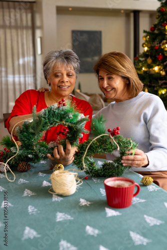 Senior female friends crafting Christmas wreaths together, enjoying festive holiday spirit, at home photo