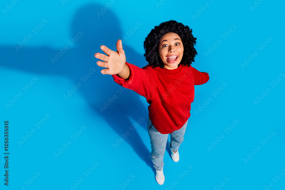Full size photo of pretty young girl top view stretch hand excited wear trendy red outfit isolated on blue color background Full size photo of pretty young girl top view stretch hand excited wear trendy red outfit isolated on blue color background