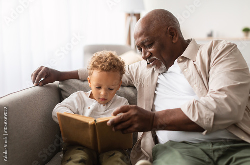 Bild auf Leinwand African American Grandpa And Grandson Reading A Book Spending Time Together Sitting On Couch At Home On Weekend