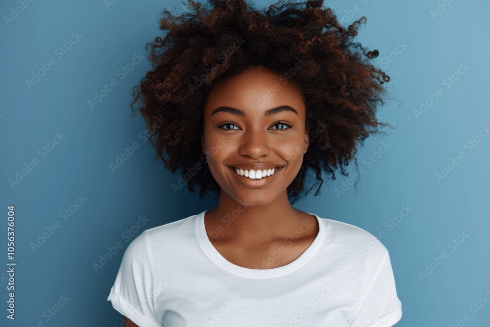 cheerful young African American woman with afro hair smiling in white t-shirt against blue background cheerful young African American woman with afro hair smiling in white t-shirt against blue background