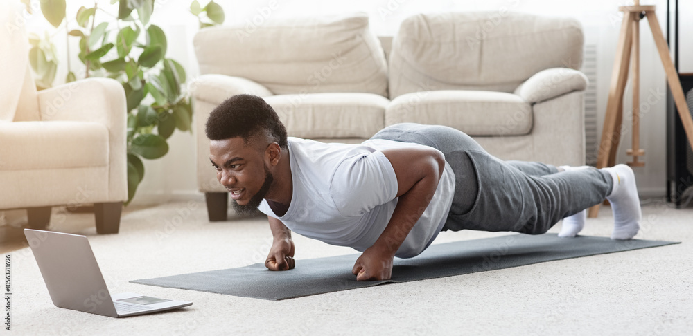 Home Workout. Sporty Young Black Man Making Fist Plank Exercise In Front Of Laptop, Watching Fitness Tutorials Online, Panorama