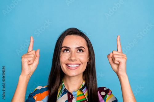 Photo portrait of attractive young woman point look up empty space dressed stylish colorful print clothes isolated on blue color background