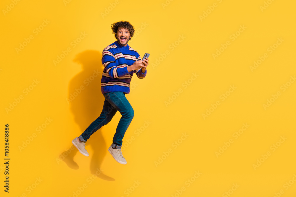 Full length photo of handsome young guy running hold gadget dressed stylish blue striped garment isolated on yellow color background Full length photo of handsome young guy running hold gadget dressed stylish blue striped garment isolated on yellow color background