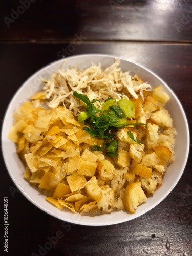 A bowl of warm chicken porridge. Indonesian food consists of white rice porridge, shredded chicken, cakwe, crackers, and leek. 