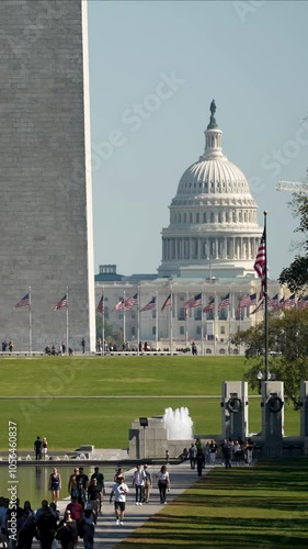 Vertical Video view of the Reflecting Pool in Washington DC with the Washington Monument, and the US Capitol in the background. People stroll along the walkway with trees lining the path