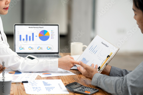 Two confident business people point to graphs and charts to analyze market data, balance sheet, account, net profit to plan new sales strategies to increase production capacity.