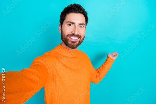 Photo of attractive handsome blogger man wear orange trendy clothes hold empty space isolated on cyan color background photo