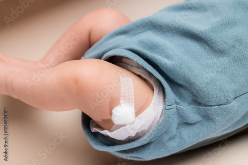 Newborn baby boy legs with a band aid patch after taking a vaccine