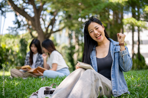 A beautiful Asian female college student sits on grass in her campus park, smiling at the camera.