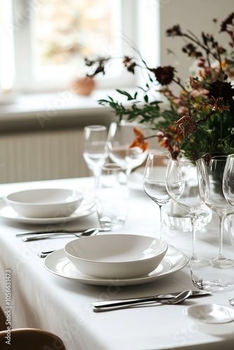 A table is set with white plates, bowls, and wine glasses