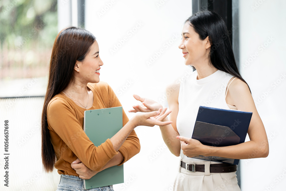 Two female collegues standing next to each other and discussing in an office Two female collegues standing next to each other and discussing in an office