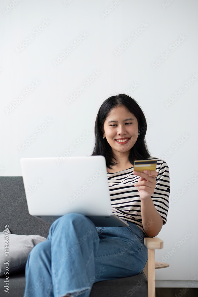 Young Woman Relaxing in Modern Living Room with Laptop and Credit Card, Smiling and Enjoying Online Shopping Young Woman Relaxing in Modern Living Room with Laptop and Credit Card, Smiling and Enjoying Online Shopping