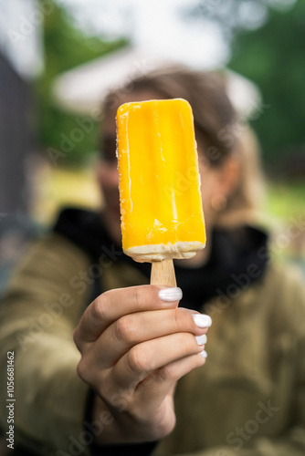 A young woman holding a yellow ice-cream on a stick photo