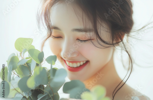 A photograph of an extremely beautiful woman in her wedding dress, smiling and holding eucalyptus flowers with the sea in the background photo