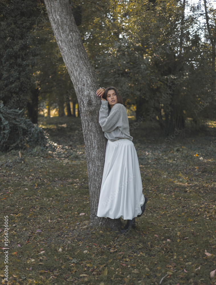 beautiful woman posing next to a tree, dressed in long skirt and wearing autumn pullover, sweater. girl hugs a tree, leaning head from brunch. female putting on black boots sitting on bent branch. beautiful woman posing next to a tree, dressed in long skirt and wearing autumn pullover, sweater. girl hugs a tree, leaning head from brunch. female putting on black boots sitting on bent branch.
