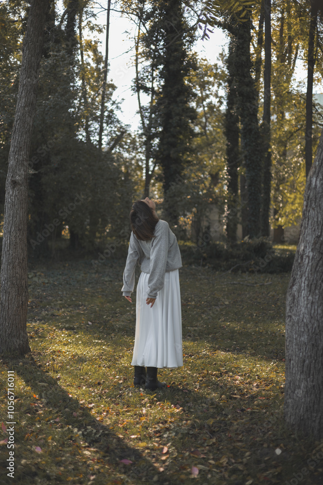 beautiful woman posing outside in park, in sun rays.girl in long white skirt dancing or running on grass, autumn fall season.female holding a leaf in hand or cover half face.sunshine on model face